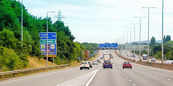 Cars driving South on the M5 Motorway near Exeter, with a sign indicating the Moto Services on the left