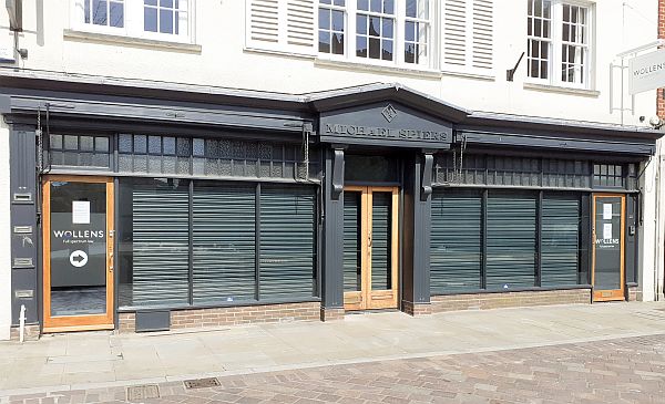 Shopfront with black perforated roller shutters closed behind windows