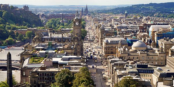 view over the city centre of Edinburgh, with a busy street, obelisk, clock tower and castle