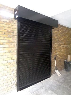 Black roller shutter closed in front of a doorway in a garage